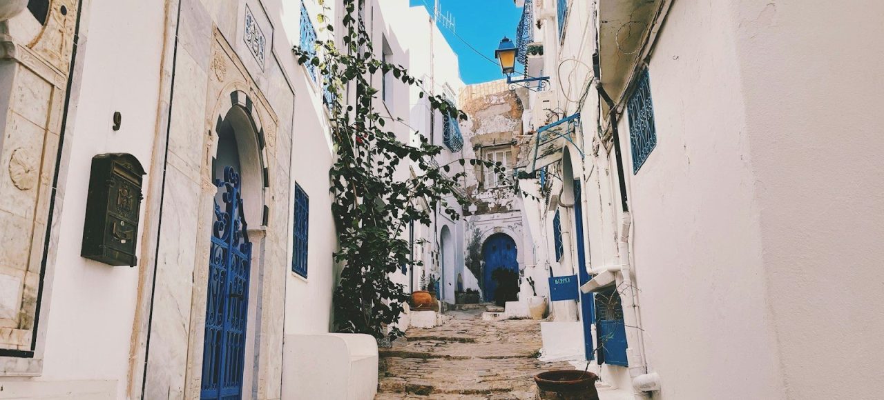a narrow cobblestone street lined with white buildings